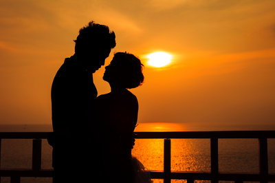 Kobieta przytulona do mężczyzny na tle zachodzącego słońca nad jeziorem