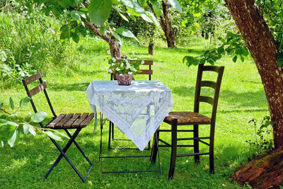 Stolik nakryty białym obrusem stojący w pięknym zielonym ogrodzie
