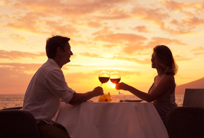 Para siedząca przy stole na tle zachodzącego słońca i pijąca wino z kieliszków